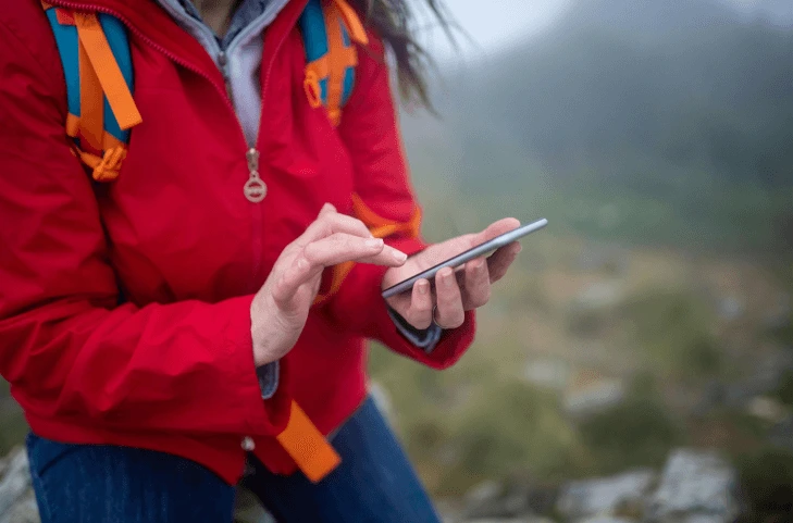 person wearing a bright red jacket searching for travel information via AI on her phone