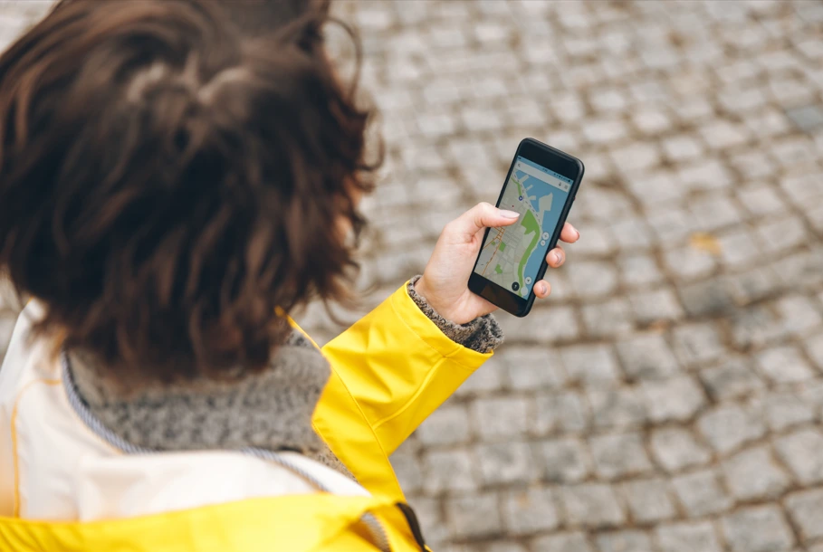 woman in yellow raincoat holding a phone with the Google Maps app open