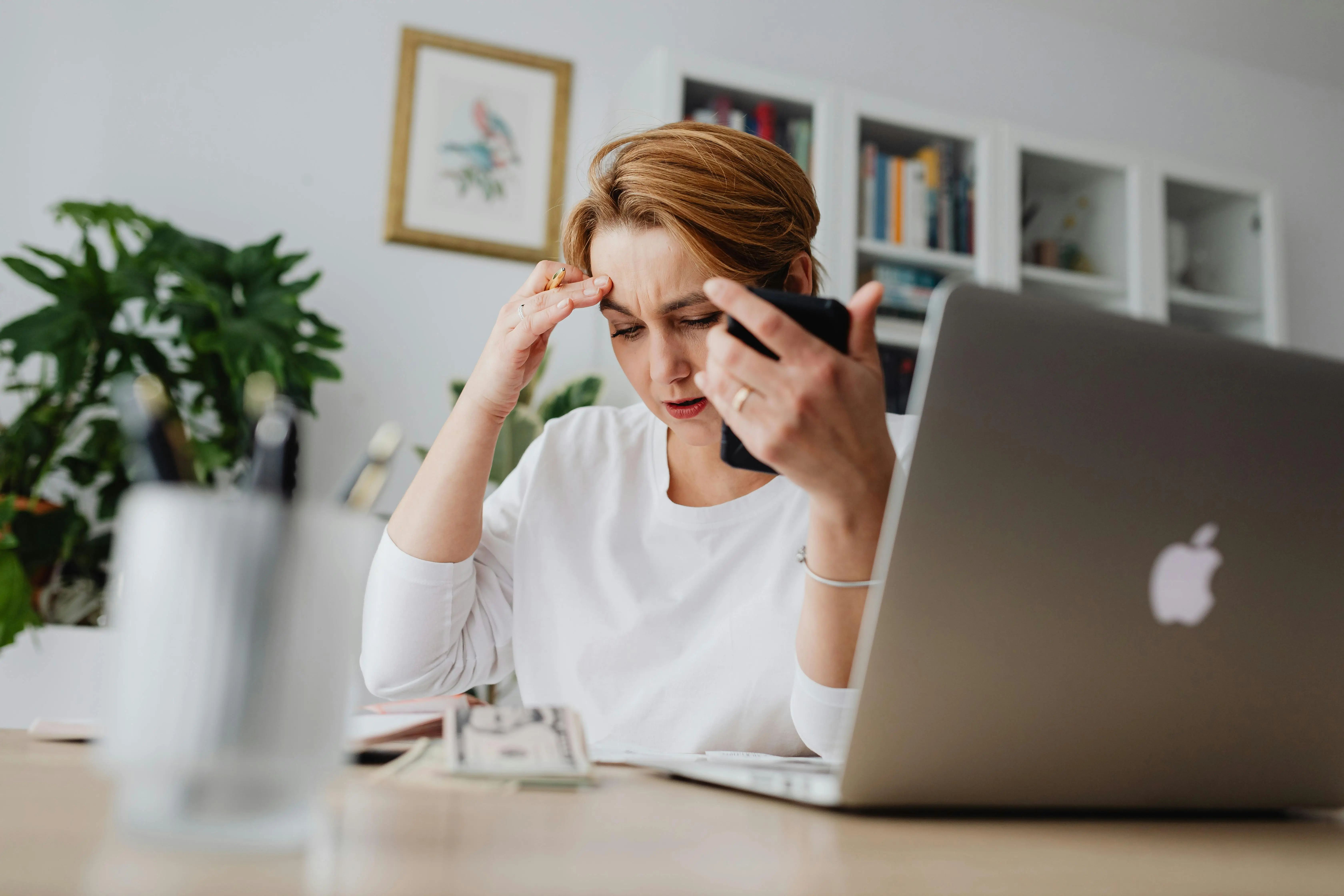 woman seemingly frustrated with her phone, sitting at a desk and looking down