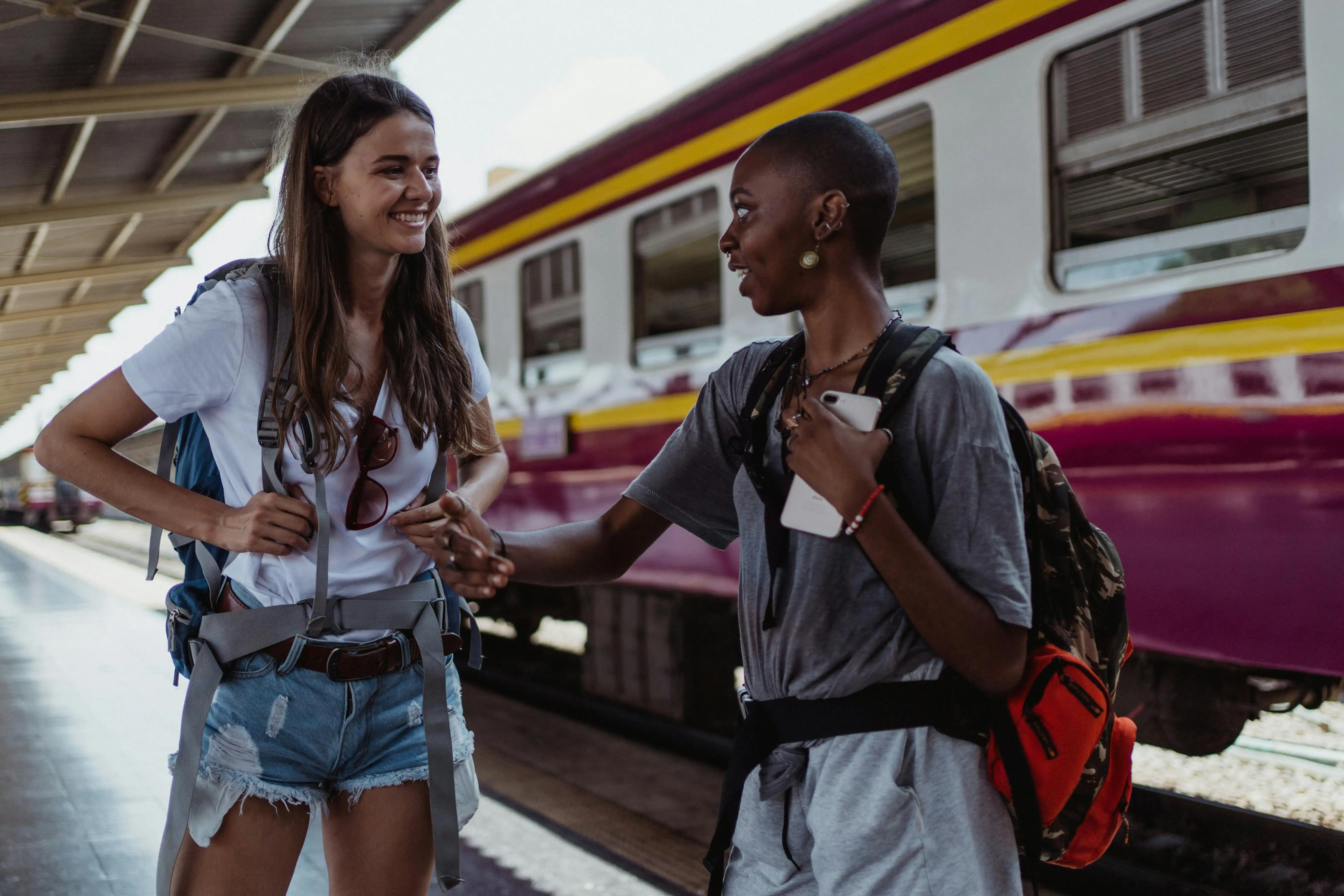 two women with travel backpacks standing at a train station while traveling