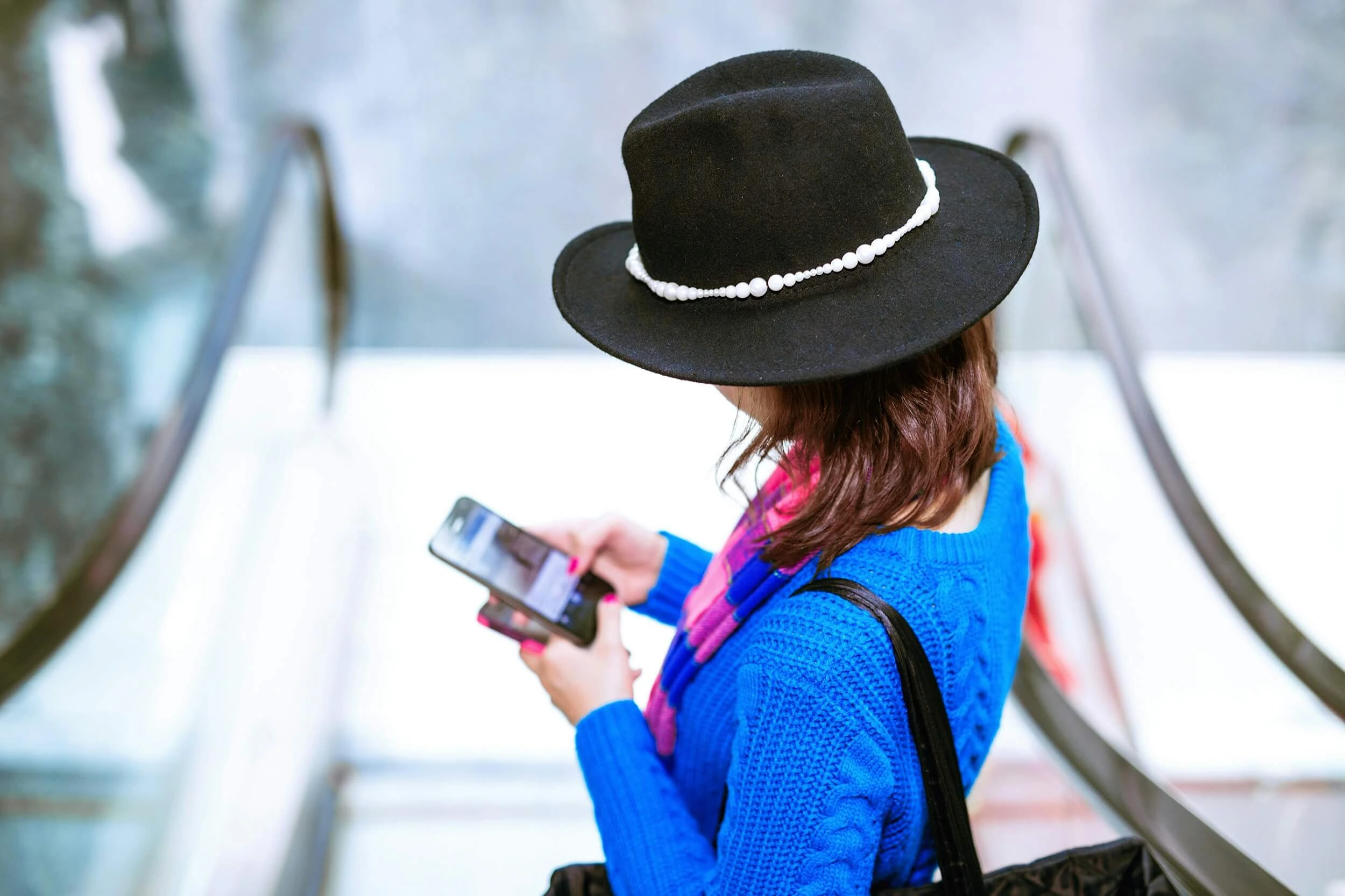 person with a black hat and blue sweater surfing on her phone while using a rechargeable esim