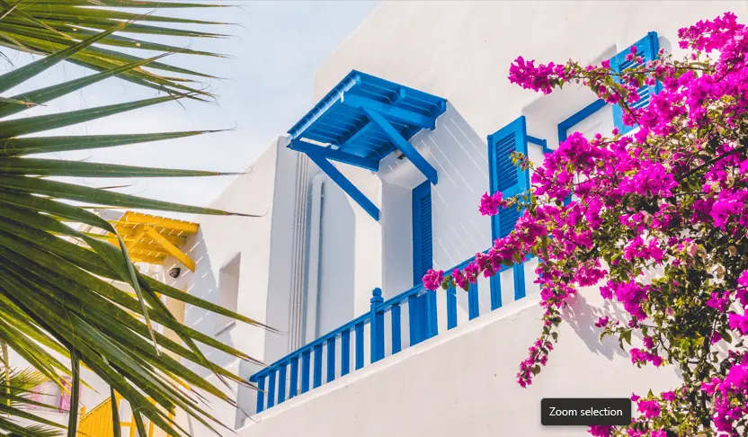 white house in Santorini with flowers and palm trees in front of it