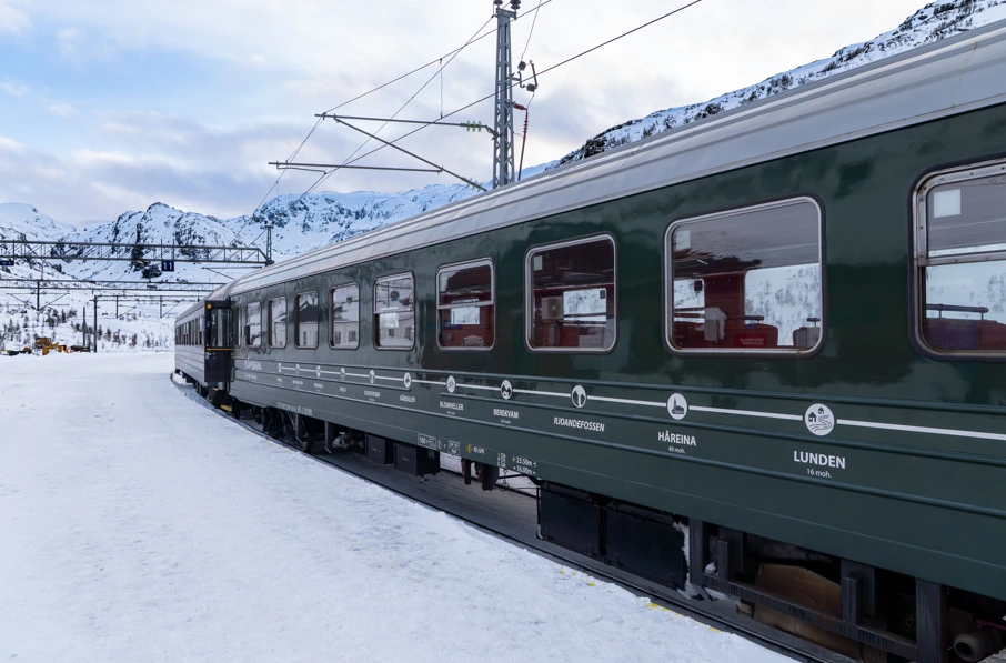green train going throw snow covered area in Norway